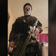 A screenshot of Sarah Beth Clendaniel dressed in military gear and holding a large gun is shown.